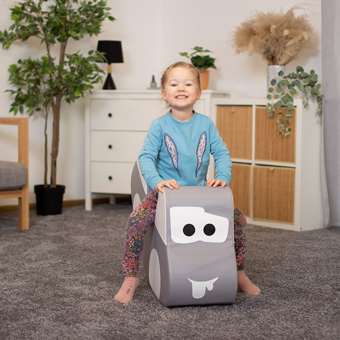 A girl sitting on a toy car rocker, smiling