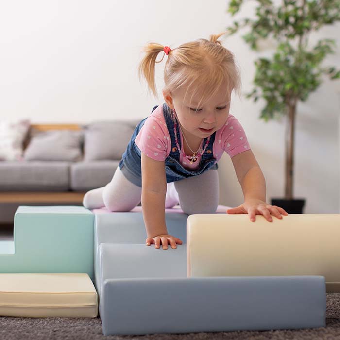 A little girl improving her motor skills by climbing on IGLU Soft Play - Explorer in a living room.