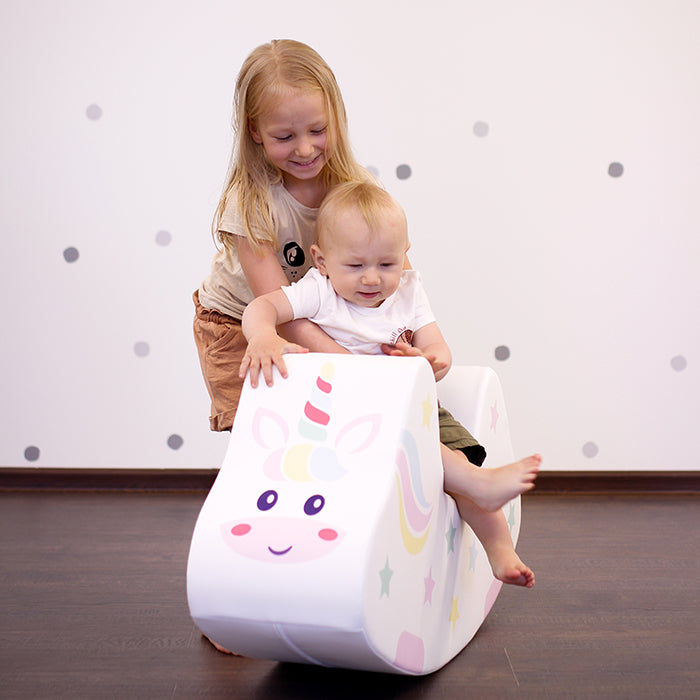 A girl helping a baby use a foam rocking toy