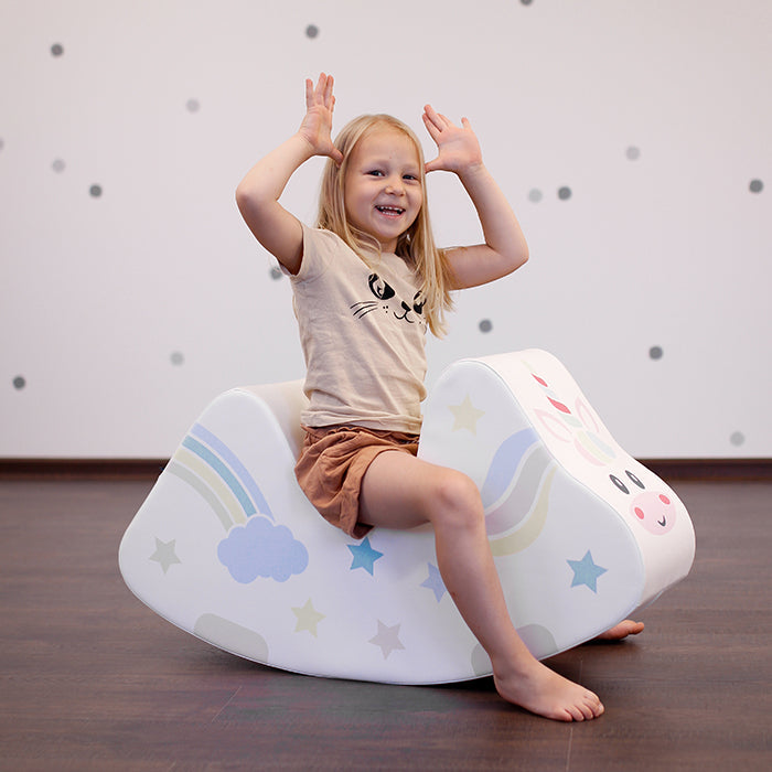 A girl rocking on a foam unicorn rocking toy