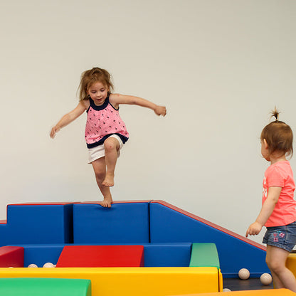 Girl jumping into a soft play ball pit by IGLU